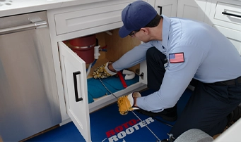Technician from Roto-Rooter performing drain cleaning in a Dallas kitchen