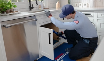 A Roto-Rooter technician is addressing a leak repair in Dallas by tightening a pipe in one hand and gripping it with a towel in the other.