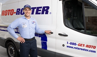Roto-Rooter technician standing outside a Roto-Rooter van with his hand on the door