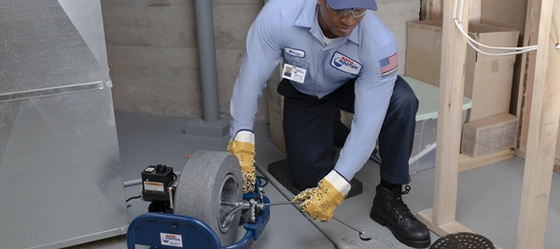 Roto-Rooter technician kneeling before a drain, preparing to do a video camera sewer inspection