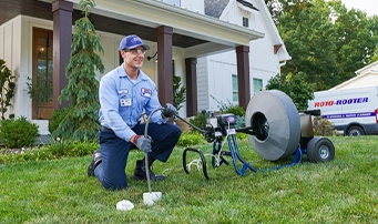 Roto-Rooter technician kneels on the front lawn of a house while doing a video camera sewer inspection in Portland