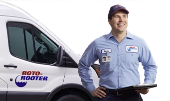 Roto-Rooter technician with clipboard in hand stands outside a Roto-Rooter truck