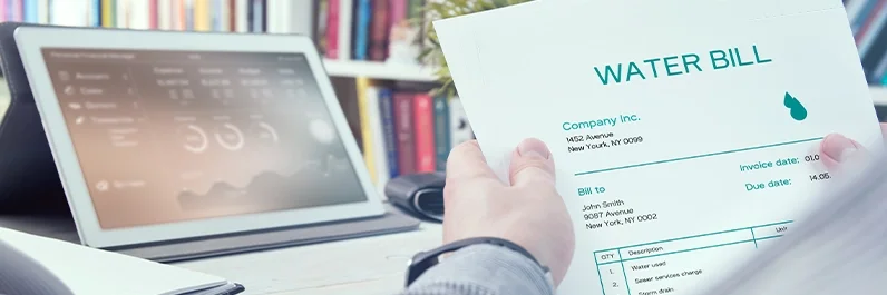 Hands holding a water bill in front of a laptop