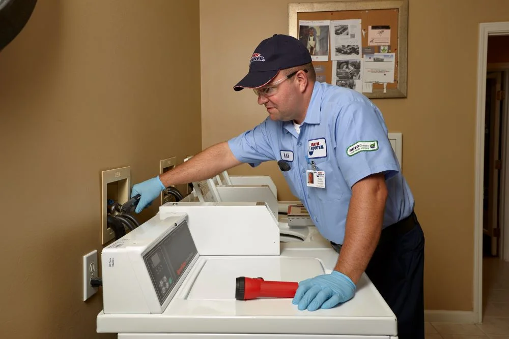 Plumber reaching over washing machine to grab connected water or drain line
