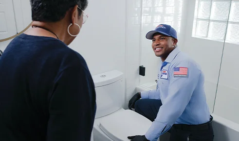 Smiling plumber informs client on issue with toilet, steps to repair